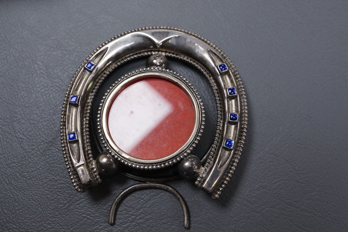 A late Victorian novelty silver and enamelled small photograph frame, modelled as a horseshoe, Birmingham, 1895, height 69mm together with a late 19th century Hanau white metal fish pin cushion(lacking cushion).